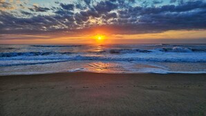 A beach with waves, a sunset, and a cloudy sky.