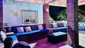 Un espace extérieur aménagé avec un canapé bleu, un pilier en briques et des guirlandes lumineuses.