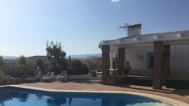Une piscine avec des chaises longues et un espace patio couvert.