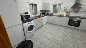 Une cuisine de taille réduite, avec des meubles blancs, un lave-linge, un four à micro-ondes, un évier et un four.