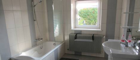 Un baño con bañera, ventana, radiador y lavamanos.