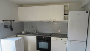 Eine kleine Küche mit weißen Schränken, einem Einbauofen, einem Geschirrspüler und einem Kühlschrank.