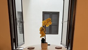 Une table ronde avec quatre chaises, un vase rempli de fleurs jaunes et une fenêtre avec des volets.