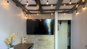 Un salon moderne avec un téléviseur à écran plat fixé à un mur en pierre, une table à manger en bois avec des chaises et un fauteuil jaune.