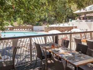 Un espace de restauration en plein air, avec des chaises et des tables en osier, donnant sur une piscine et des chaises longues.