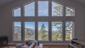 Un amplio salón con techo alto y ventanas grandes que ofrecen vistas a una cadena montañosa boscosa.