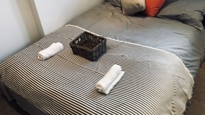 Un lit avec une literie à rayures, un panier noir et des serviettes enroulées.