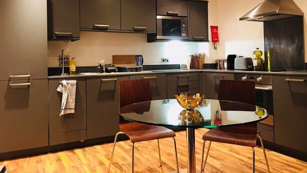 Une cuisine moderne avec des meubles de couleur sombre, un îlot central doté de tabourets et un micro-ondes placé au-dessus de l’îlot.