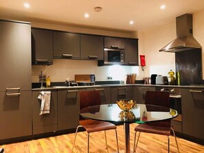 A modern kitchen with dark cabinets, a central island with stools, and a microwave above the island. - 2bed 2bath apartment in kings cross (London)
