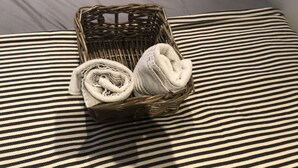 Un panier en osier contenant des serviettes enroulées, posé sur un coussin à rayures.