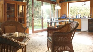 Un vaste espace de vie aménagé avec des meubles en osier, une table à manger et un coin cuisine doté d’une fenêtre donnant sur un espace verdoyant.