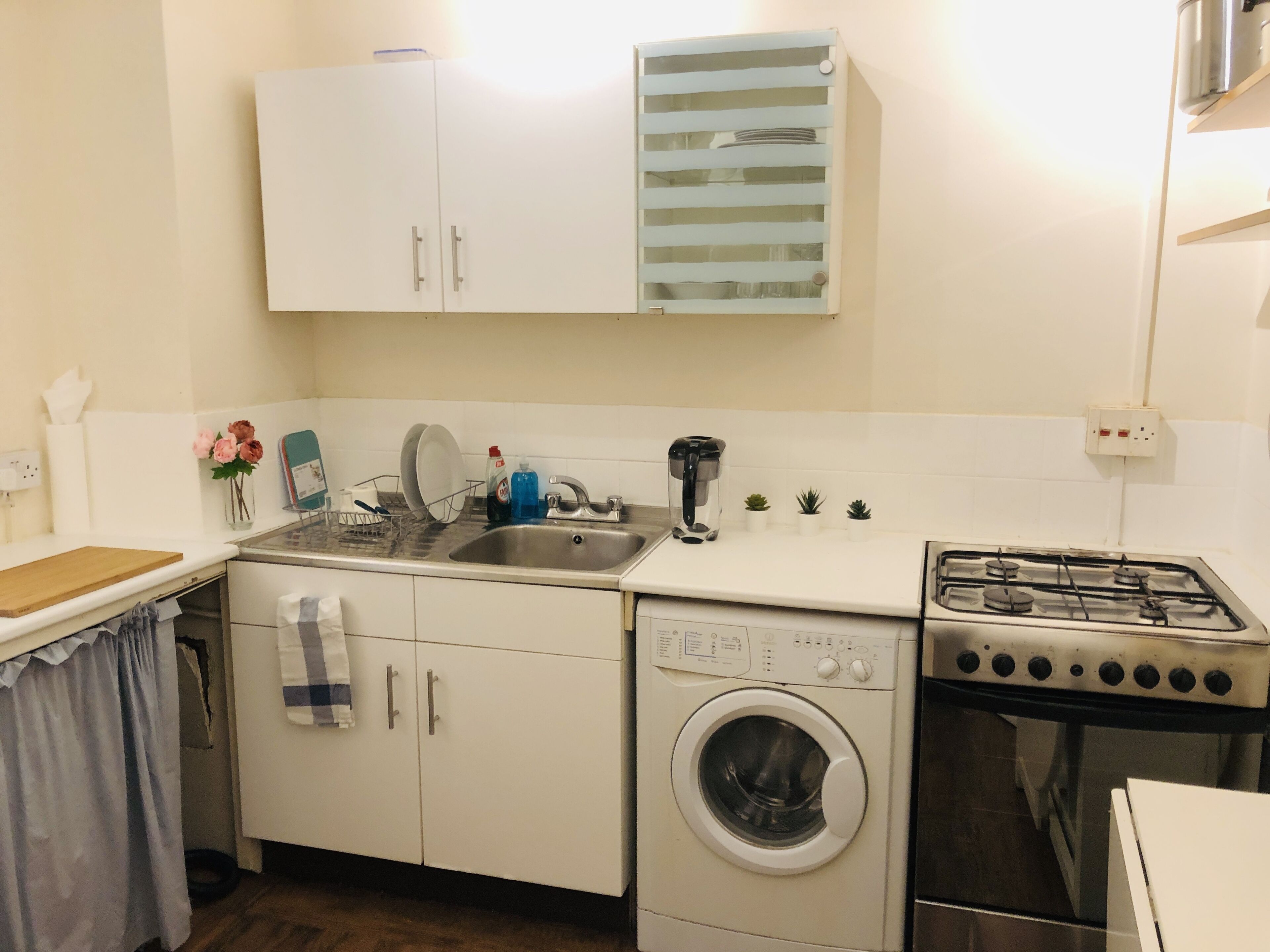 A compact kitchen with a washing machine, a stove, a sink, and cabinets.
