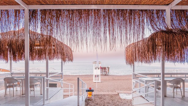 Eine Terrasse direkt am Strand mit weißer Möbel, einem Rettungsturm und Blick auf den Ozean.