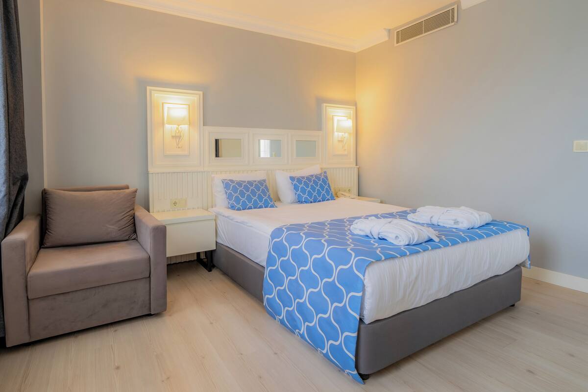 A hotel room with a bed, a chair, bedside tables, and wall-mounted lamps.
