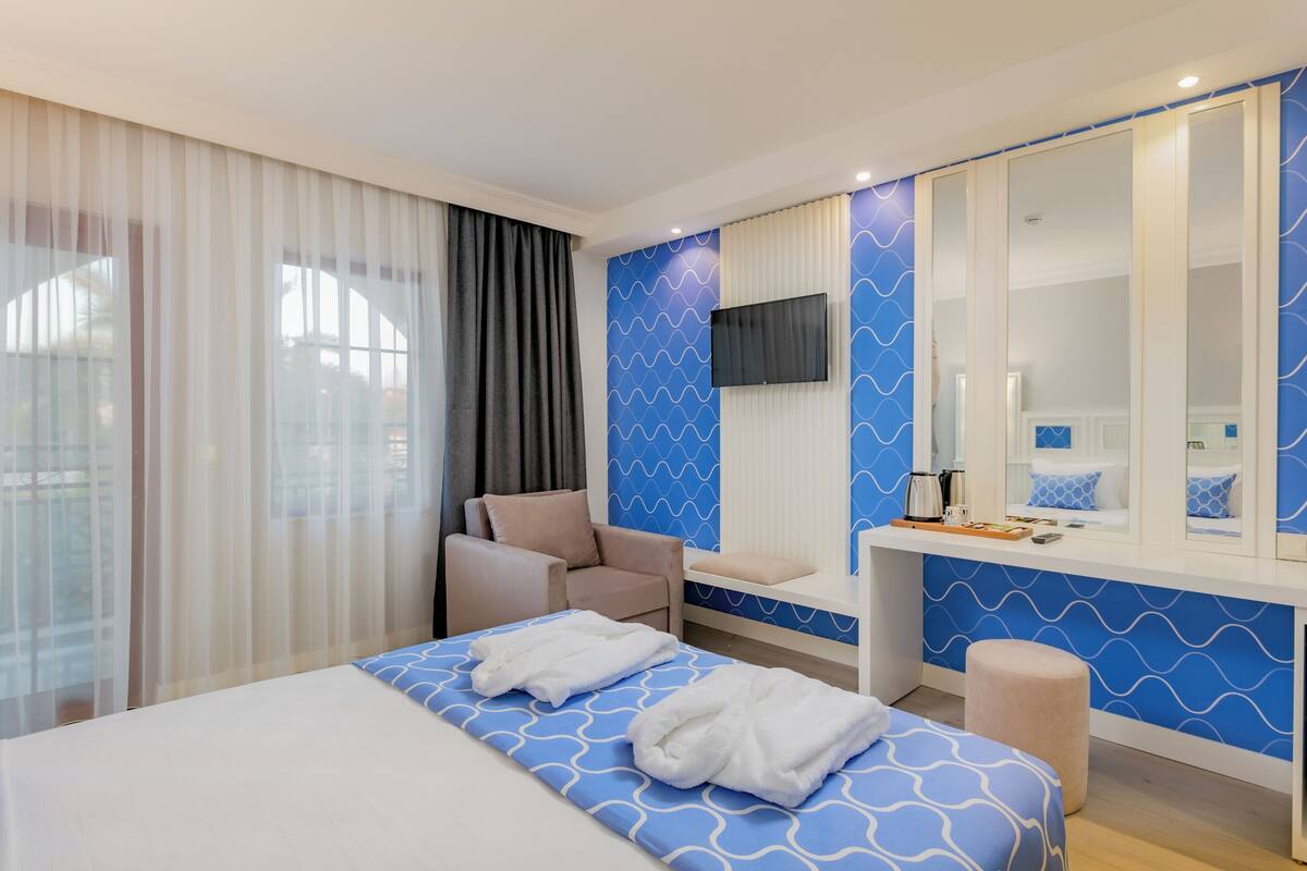 A hotel room with a bed, a seating area, a vanity with a mirror, and a television.