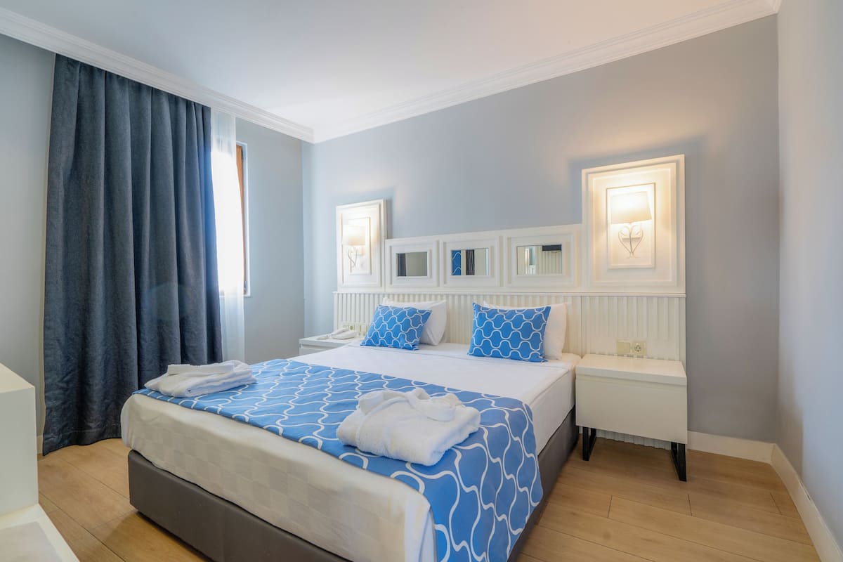 A hotel room with a bed, a nightstand, a bedside table, and a window with curtains.