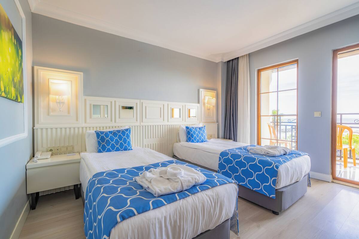 A hotel room with two beds, a nightstand, a lamp, a painting, and a balcony.
