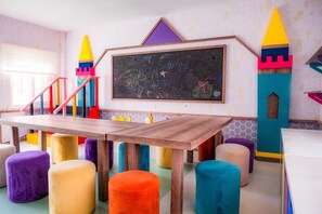 Un cuarto de juegos infantil con una mesa de madera, taburetes de colores y una pared con pizarra.