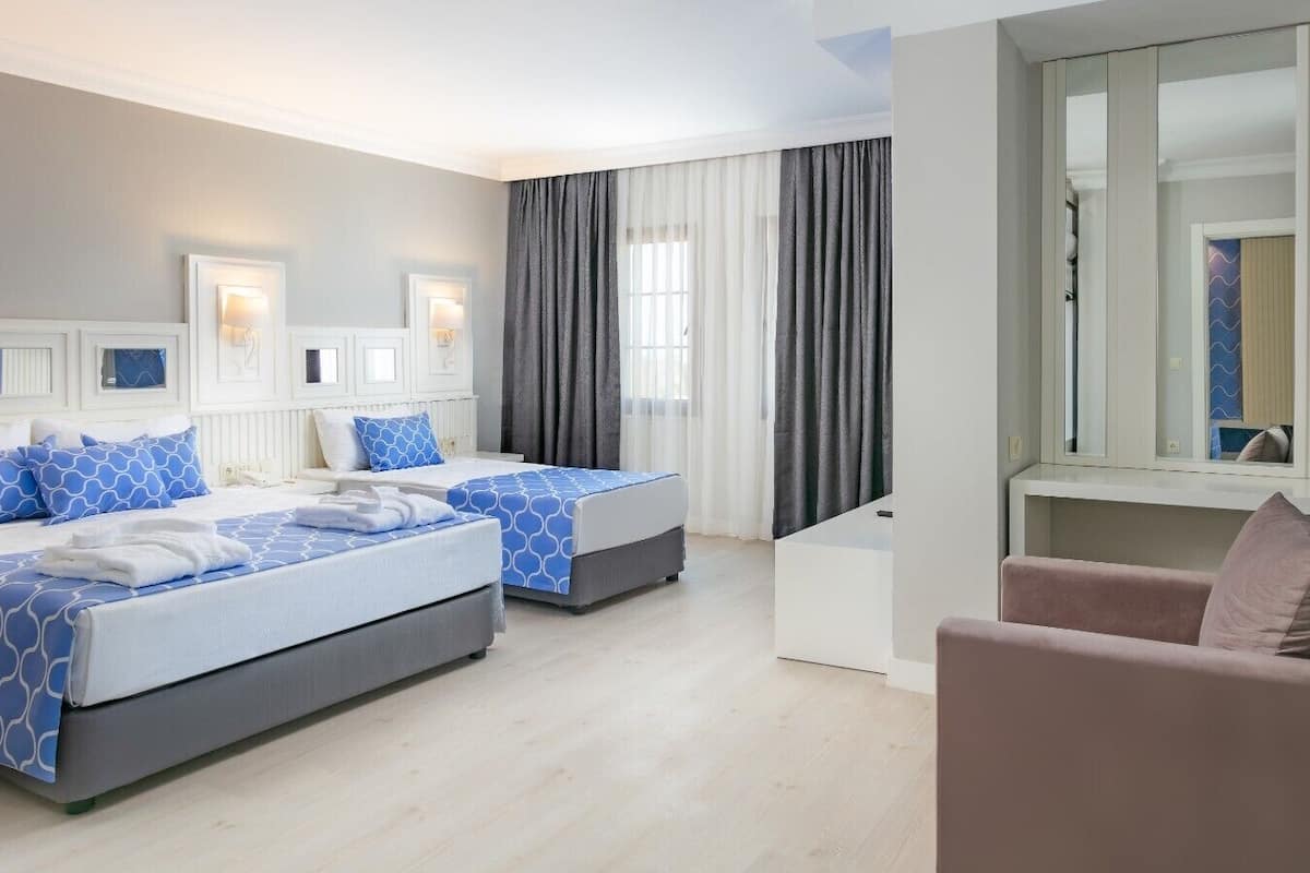 A hotel room with two beds, a sofa, a desk, and a large window with curtains.