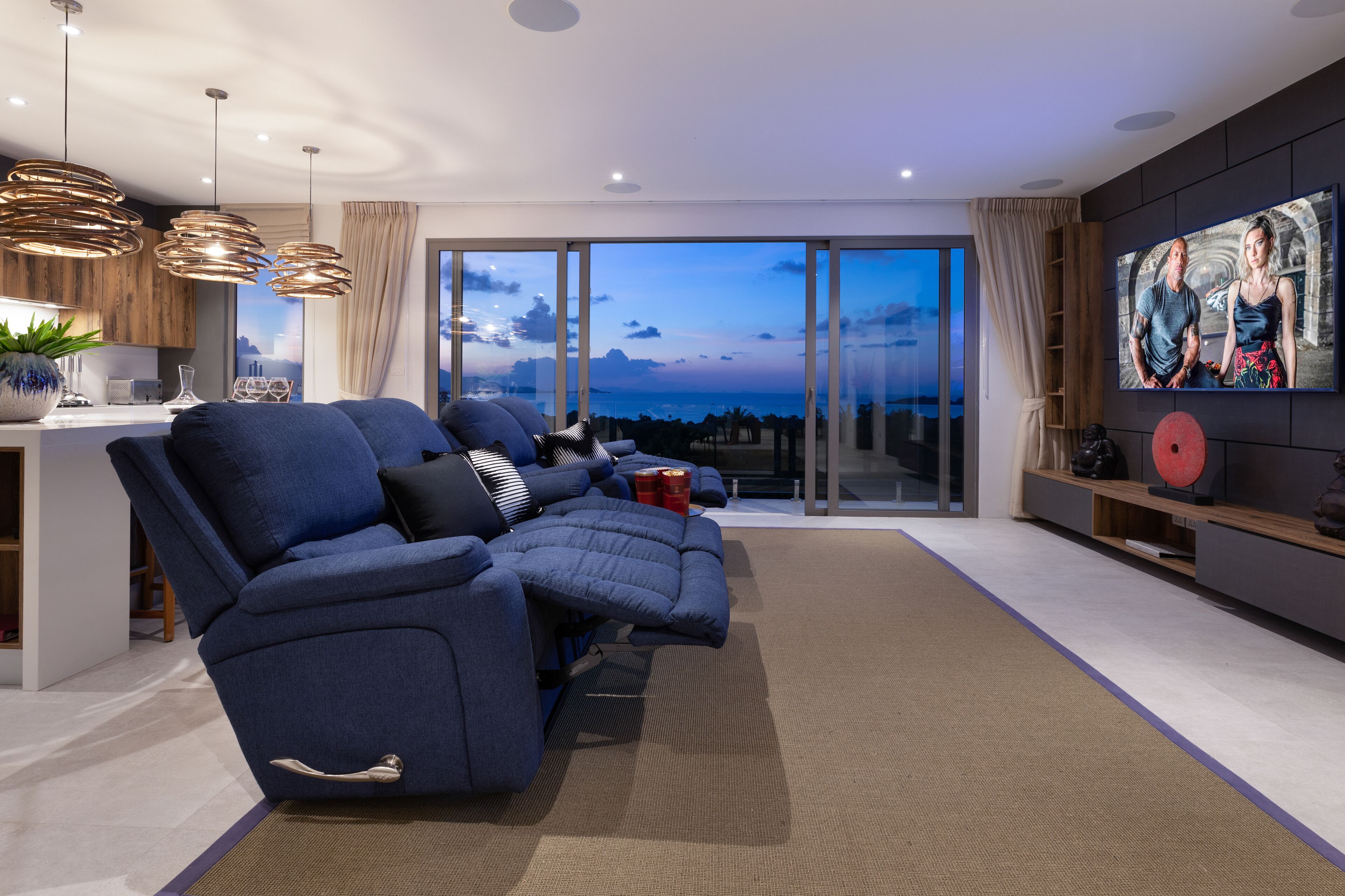 Een moderne woonkamer met een modulaire bank, een keukenhoek en een grote schuifpui die uitkomt op een balkon met uitzicht op de stad.