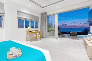A modern hotel room with a large bed, a desk with a chair, and a balcony with a view of the sea. - Samui Sunsets Luxury Villas (Koh Samui)