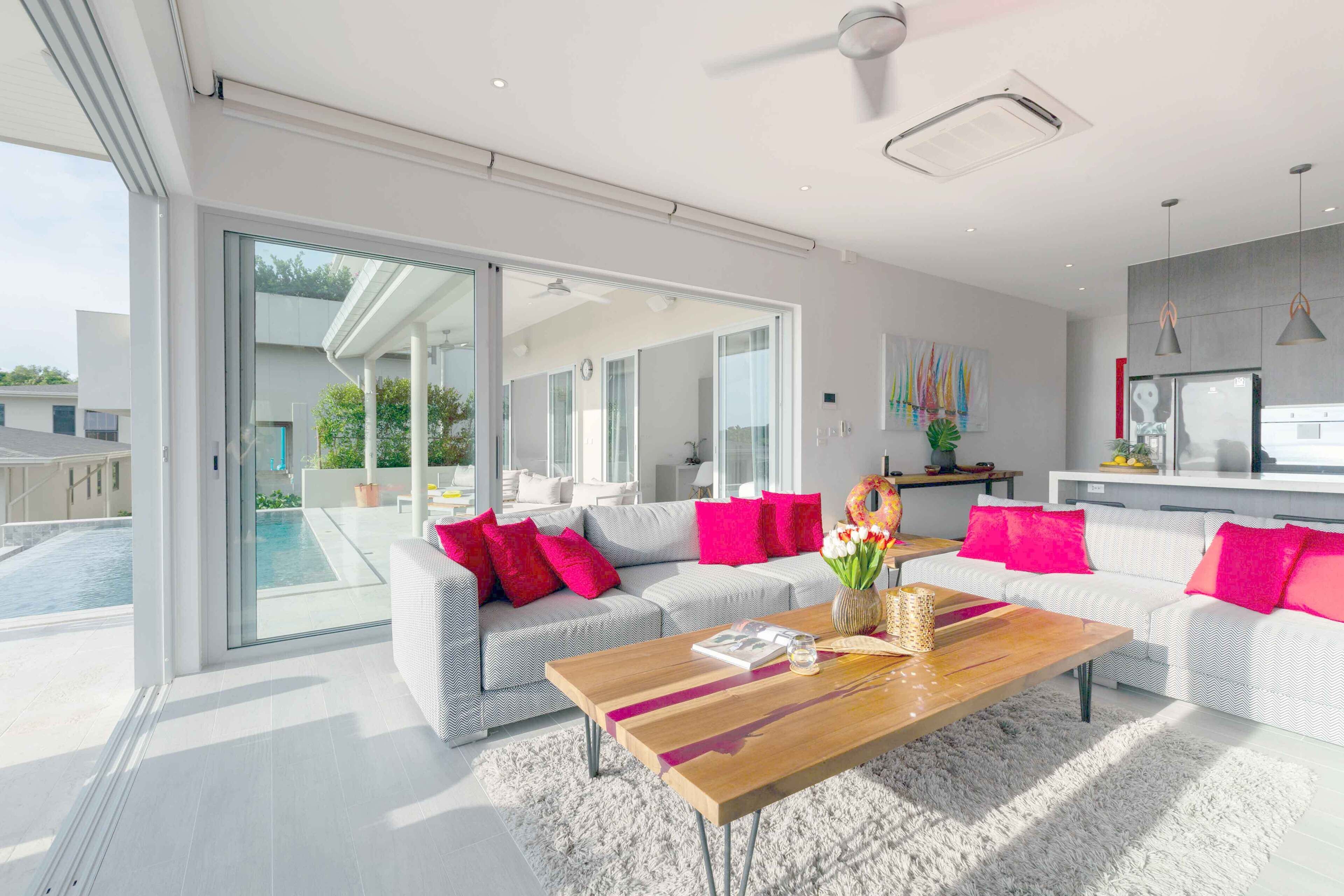 A modern living room with a large sofa, a coffee table, and a view of a swimming pool and outdoor area.