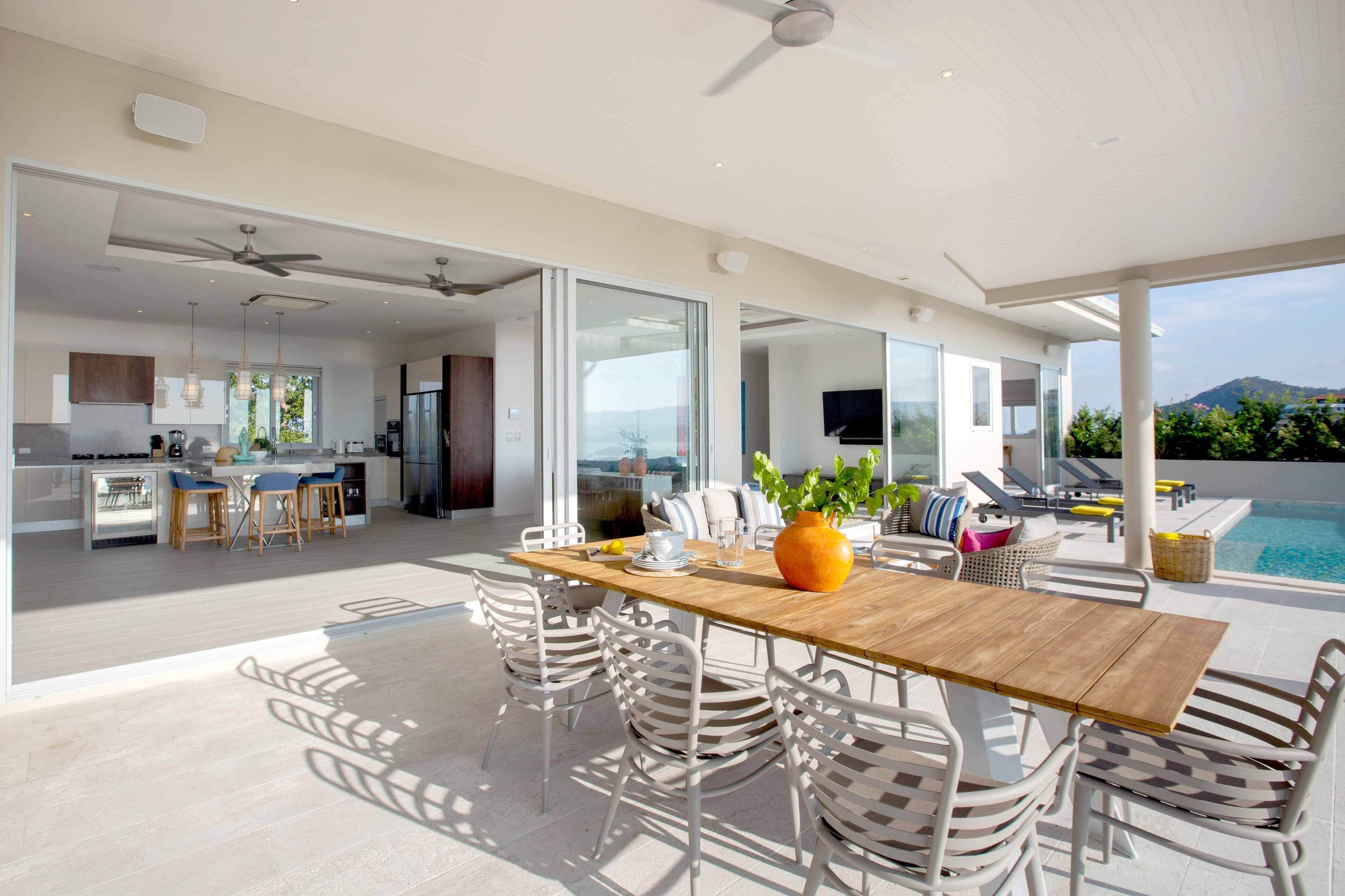 A modern open-plan living space with a dining area, kitchen, and a poolside lounge.