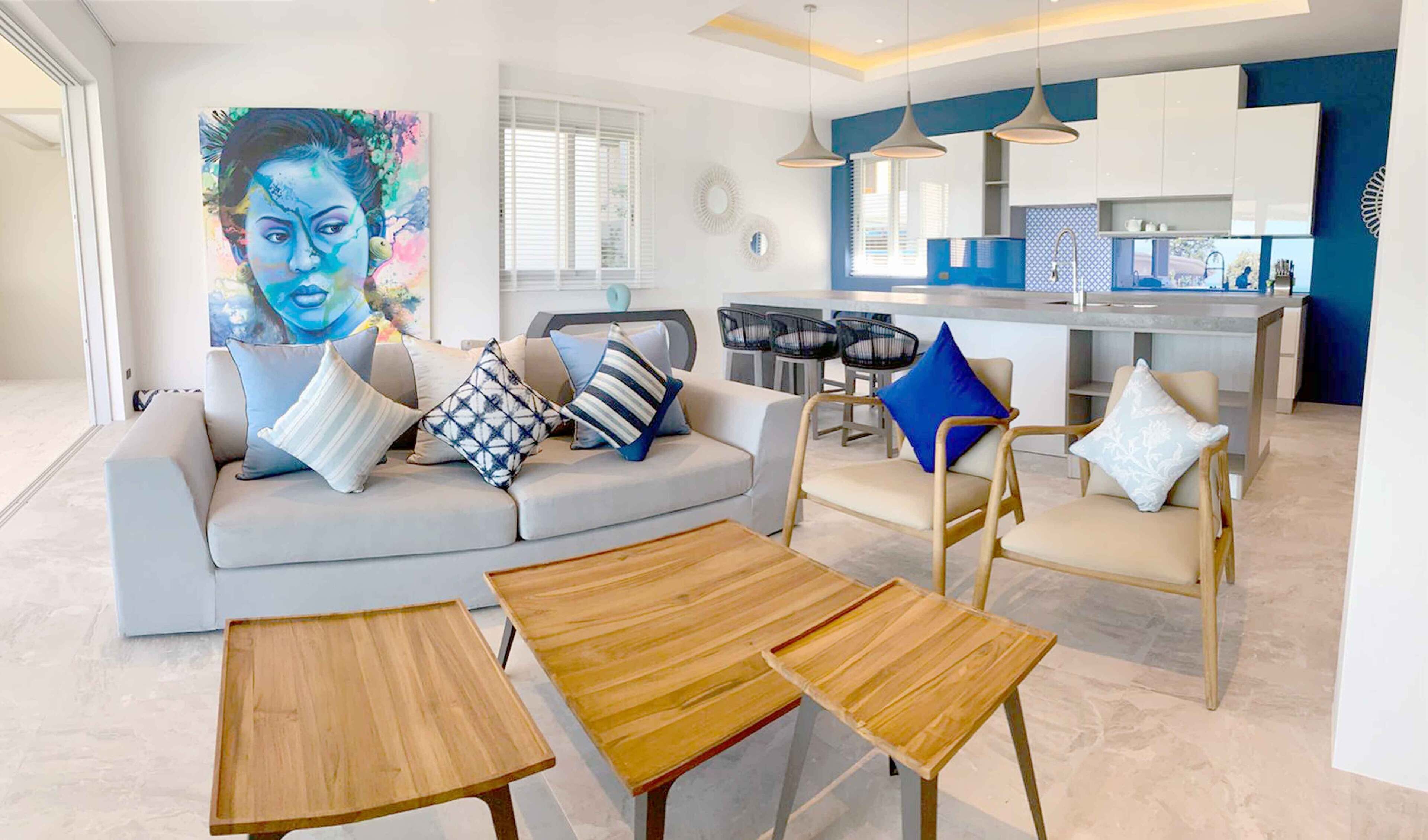 A modern living room with a sofa, coffee table, and chairs, a kitchen area with a dining set, and a large painting on the wall.