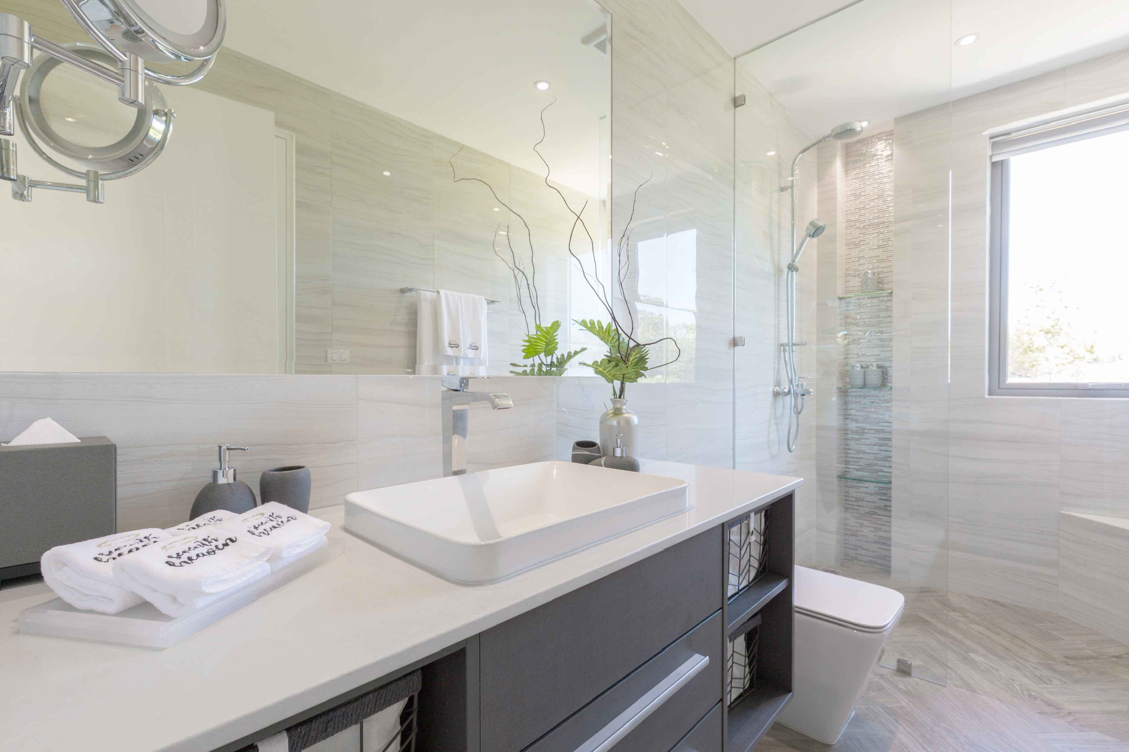 Un bagno moderno con uno specchio grande, un lavandino bianco e uno spazio doccia in vetro.