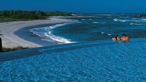 Una piscina infinita con vista al océano y a una playa de arena.