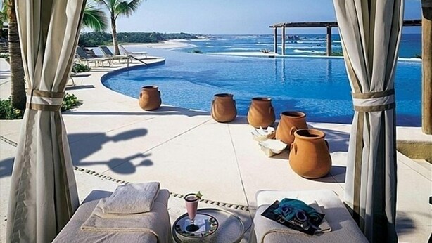 Un área de descanso junto a la piscina con vista al océano, sillas de sol y maceteros decorativos.