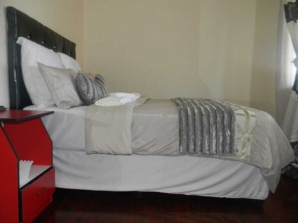 A bed with a headboard, pillows, a blanket, and a red nightstand with a drawer.