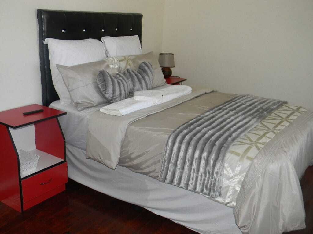 A neatly made bed with a grey and white duvet, a red nightstand with a lamp, and a wooden floor.