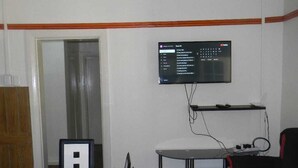 A room with a glass table, a red and black chair, a mounted TV, and a door. - M2T Guest House (Cape Town)