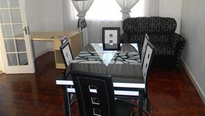 A compact living space with a dining table and chairs, a patterned sofa, and a small cabinet. - M2T Guest House (Cape Town)