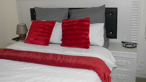 A bed with a white and red bedspread, grey and red pillows, and a white headboard. - M2T Guest House (Cape Town)