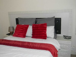 A bed with a white and red bedspread, grey and red pillows, and a white headboard. - M2T Guest House (Cape Town)