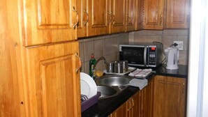 A kitchen with wooden cabinets, a microwave, a sink, and a kettle. - M2T Guest House (Cape Town)