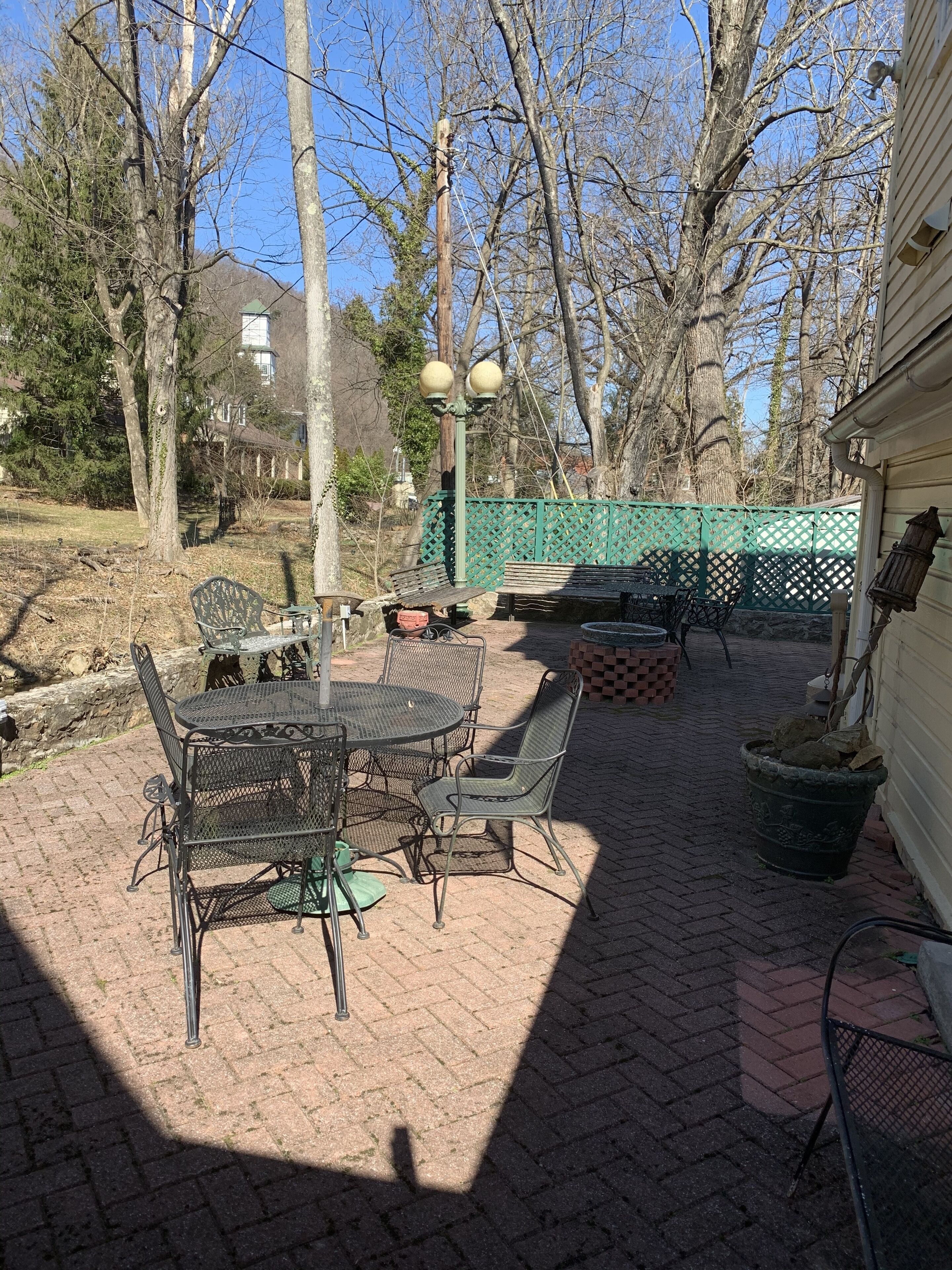 Une terrasse extérieure avec une table et des chaises en métal, un chemin en briques et une clôture verte.