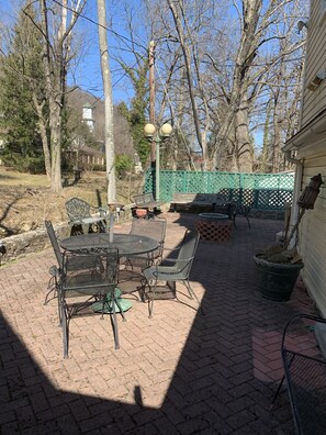 An outdoor patio with a metal table and chairs, a brick pathway, and a green fence. - Brookside Cottage is a beautiful open concept doll house stay for two. (Berkeley Springs)