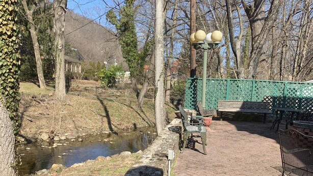 A paved area with a metal bench, a green fence, and a lamppost with spherical lights. - Brookside Cottage is a beautiful open concept doll house stay for two. (Berkeley Springs)