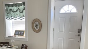 A room with a dining table, chairs, a window with curtains, a door with a small window, and a doormat. - Brookside Cottage is a beautiful open concept doll house stay for two. (Berkeley Springs)