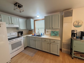 A kitchen with light blue cabinets, a white refrigerator, a stove, a sink, and a coffee maker.