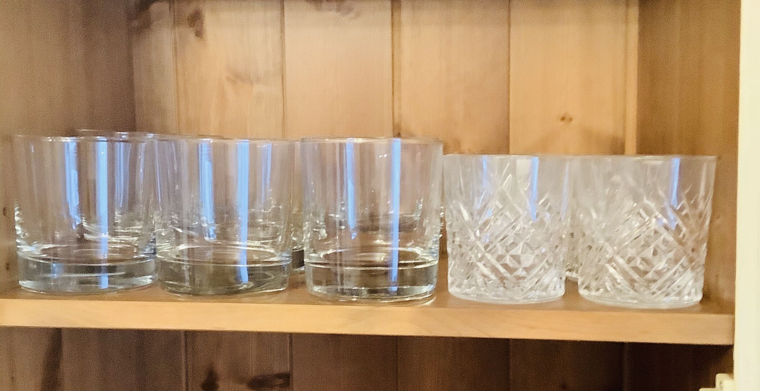 A wooden shelf with six clear glass tumblers, some with a textured pattern.