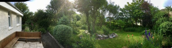 A garden with a wooden bench, a stone pathway, and various plants and flowers.
