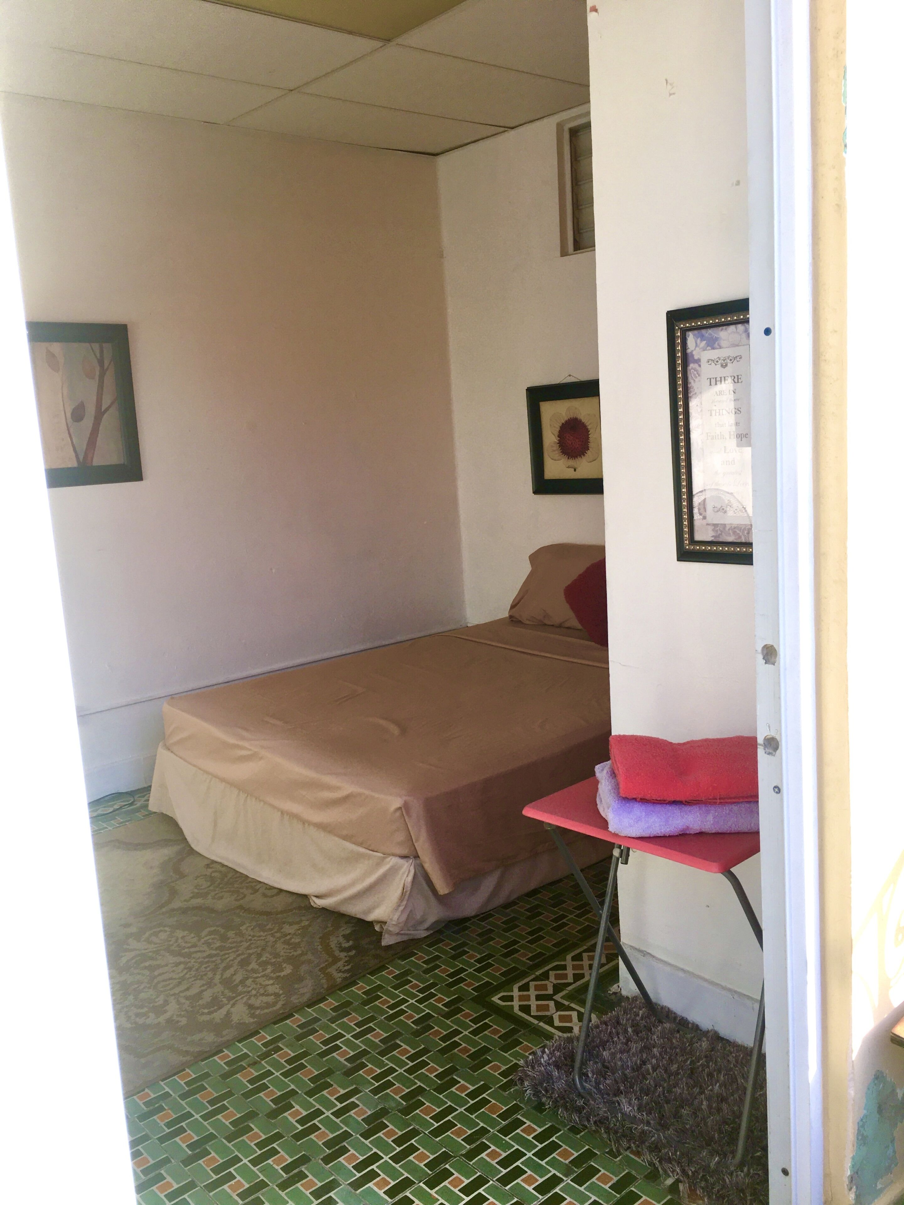 Une petite chambre avec un lit simple, un mur uni, un tableau encadré et une petite table avec des serviettes.