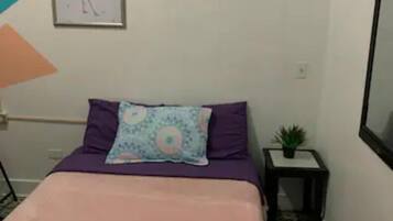 Quarto com uma cama, um travesseiro, uma planta pequena e um quadro na parede.