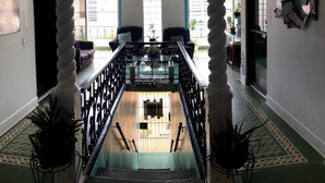 A grand staircase with ornate columns, a view of the lower level, and a balcony with potted plants. - Medusas Hostel (Aguadilla)