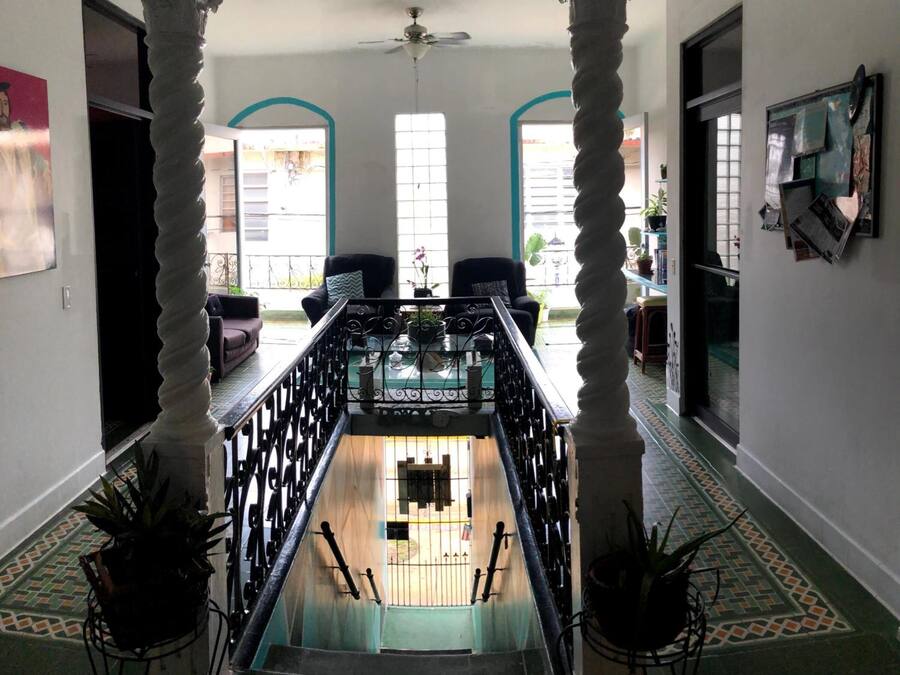 Una gran escalera con columnas ornamentales, vista del nivel inferior y un balcón con plantas en macetas.