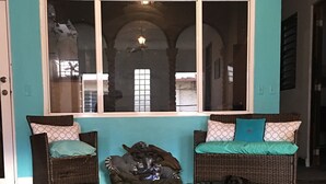 A room with two wicker sofas with patterned cushions, a dark rug, and a tiled floor. - Medusas Hostel (Aguadilla)